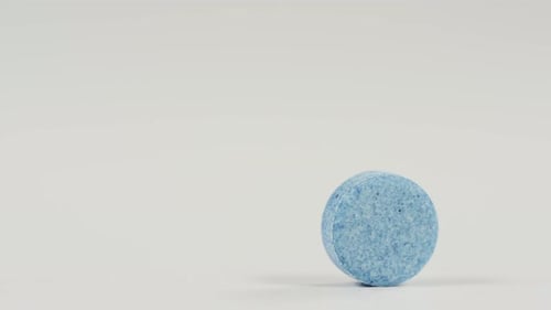 Blue Pill Moved By Hand on White Surface