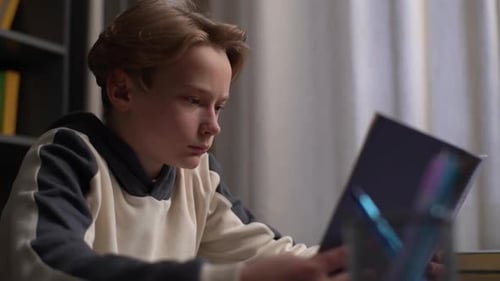Teen Boy Reading Book Indoors at Desk