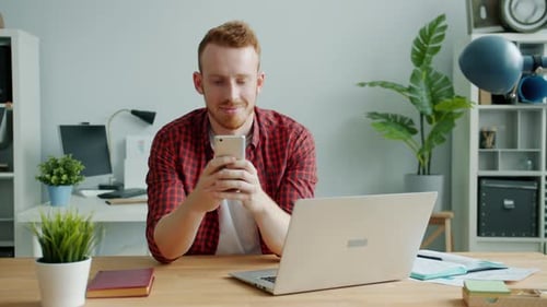 Attractive Guy Communicating with Modern Smartphone Smiling in Office Alone