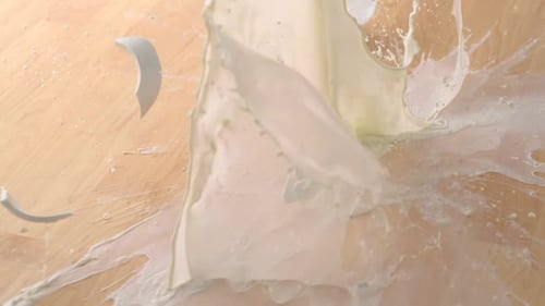 White Mug Shatters, Milk Splashes on Wooden Floor