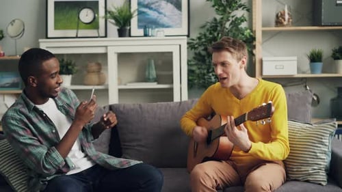 Two Young Men Play Guitar Together on Couch