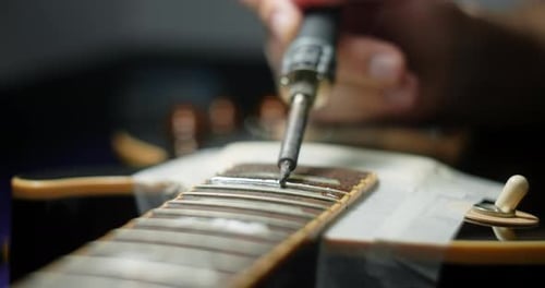 Luthier calienta los trastes de la guitarra soldando el hierro antes de refrescar los preparativos del artesano de la guitarra para