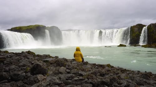 Tourist in a Yellow Jacket Relaxing at the Godafoss Waterfall in Iceland