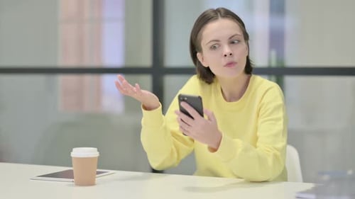 Woman Reacts to Smartphone News at Desk