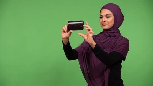 A Young Beautiful Muslim Woman Takes Pictures with a Smartphone Green Screen Background