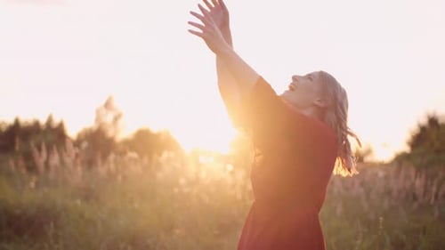 Woman in Red Dress Enjoys Sunset in Field