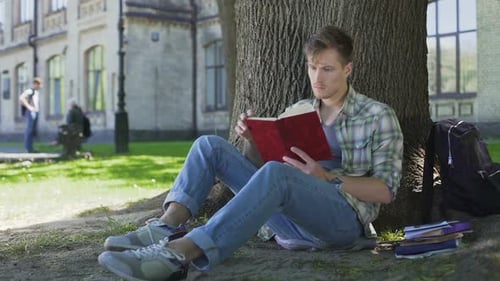 Étudiant de sexe masculin parcourant les pages du manuel, répétant le matériel appris