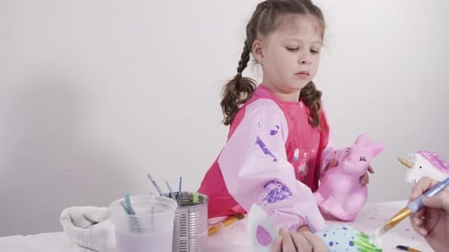 Little girl painting paper mache figurines with acrylic paint for her homeschooling art project.