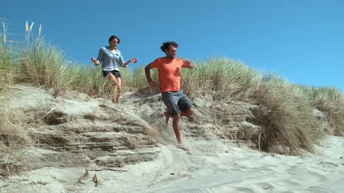 Couple at beach running down sand dune in super slow motion