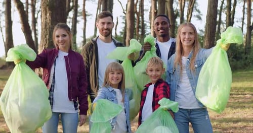 Volunteers Smiling While Holding Trash Bags in Forest