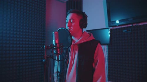 A Man in Headphones Rapping in the Studio Gesticulates While Recording His Track - Neon Lighting
