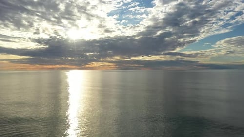 AERIAL: Flying Into the Horizon During Golden Hour with Sun Hidding Behind the Clouds