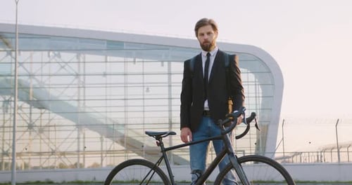 Empleado de oficina posando cerca de su bicicleta sobre el fondo de una construcción de cristal