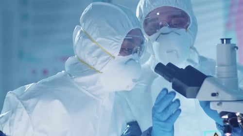 Two Scientists in Protective Uniform Using Microscope in Laboratory