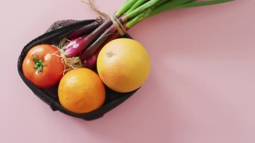 Vídeo de frutas y verduras frescas en bolsa negra sobre fondo rosa