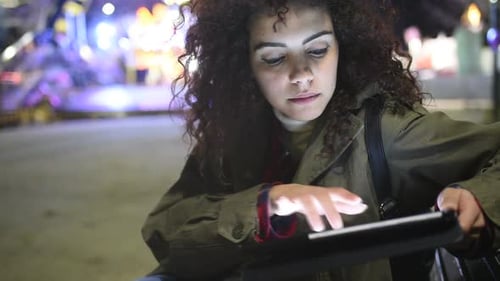 Young beautiful mixed race woman outdoor in the city night using tablet