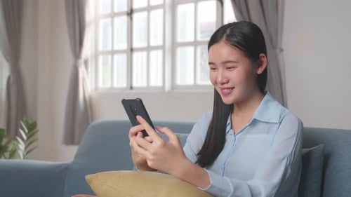 Smiling Woman Using Mobile Phone on Sofa