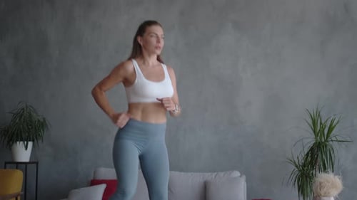 A Woman Works Out at Home in Sportswear Using a Mini Trampoline.
