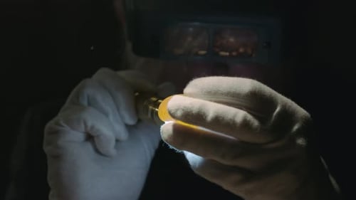 Hand Inspecting Yellow Gem Under Magnification