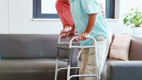 Senior Man Using Walker Assisted by Woman