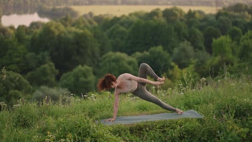 A Young Woman Does Yoga Exercises Standing on the Top of a Forest Mountain Against the Background of