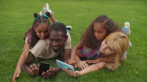Cheerful Family Lying on Grass Looking at Phones