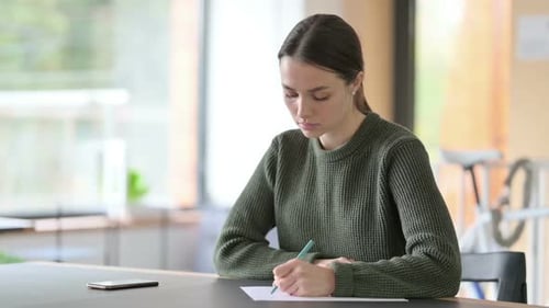 Young Adult Writing on Paper at Desk