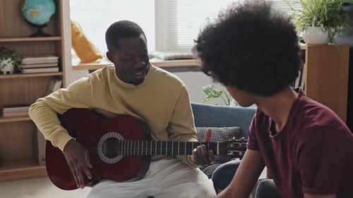 Man Plays Guitar for Friend in Living Room