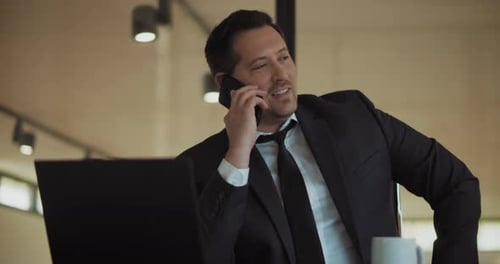 A man in a formal suit talking on the phone, while working at the office. Medium shot, slow motion.