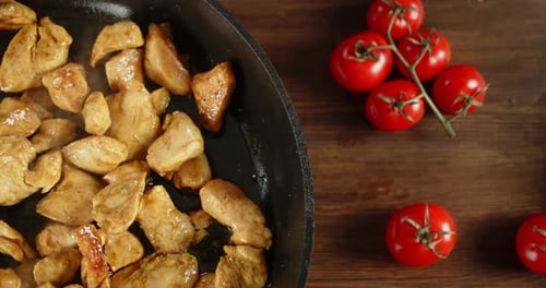 Cooking Chicken in Skillet with Tomatoes on Wood
