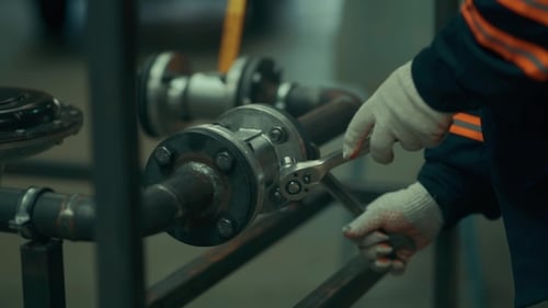 Factory Worker Tightening Bolts on Industrial Pipes