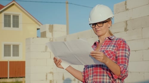 Eine Ingenieurin studiert eine Zeichnung. Es steht auf der Baustelle eines kleinen Häuschens