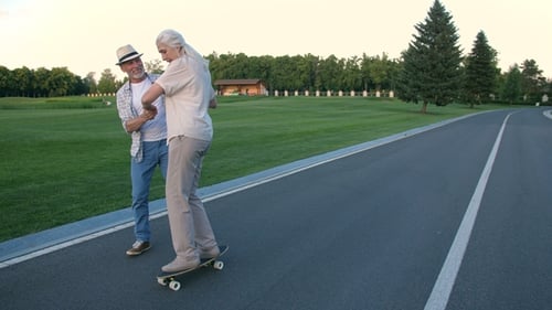 Husband Teaching Wife To Skateboard in Summer Park