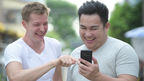 Young Adults Laughing and Using Phone Together Outside