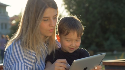 Child with Tablet and Mother on a Bench in the Park