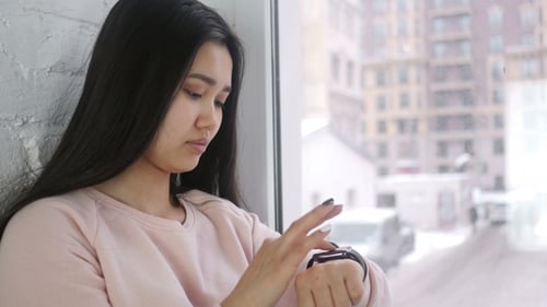 Woman Using Smartwatch by Snowy City Window