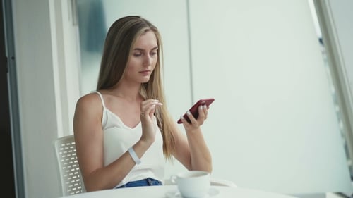 Pretty Girl Drinks Coffee, Using Smartphone in the Comfortable Light Cafe