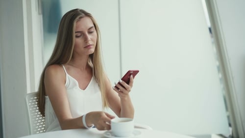 Pretty Girl Drinks Coffee, Using Smartphone in the Comfortable Light Cafe