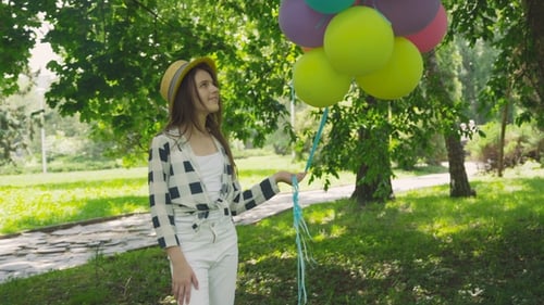 Portrait of Pretty Girl Poses at Camera with Colourful Balloons in Sunny Park