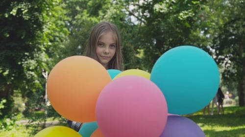 Happy Young Girl Rejoicing and Spinning with Colourful Balloons in a Park