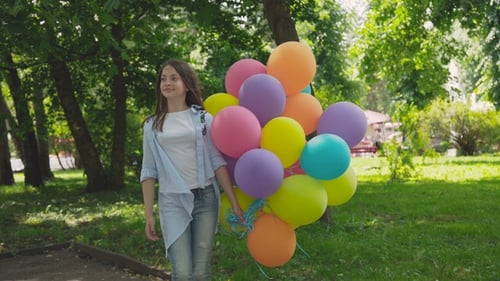 Portrait of Happy Girl Poses and Turns Around at Camera with Balloons in Park