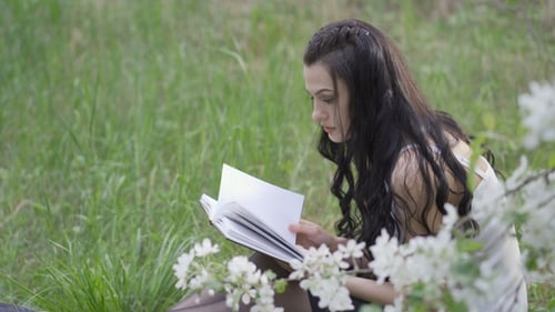 Young Woman Sitting and Reading a Book in the Park