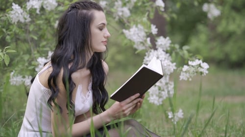 Young Woman Reading a Book in Spring Meadow