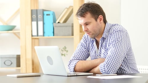 Man Smiling at Laptop in Bright Office Setting