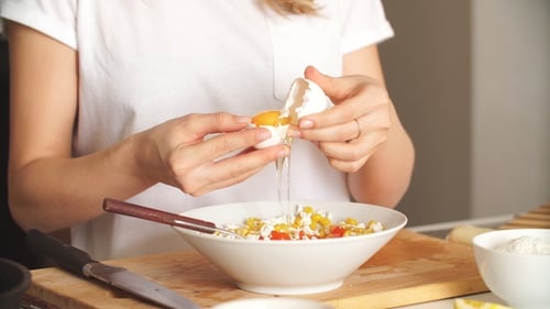 Cracking Egg Into Bowl of Vegetables in Kitchen