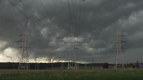 Electrical Towers Stand Beneath Stormy Sky in Field