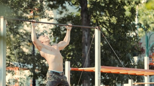 Atleta fuerte haciendo dominadas en la barra en el campo de deportes