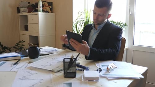 Successful Businessman Looking at Diagrams with Statistics on Papers While Working on Digital Device