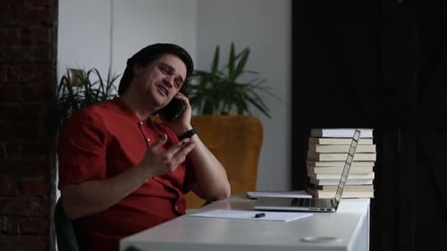 Man working at home office at laptop and talking by mobile phone