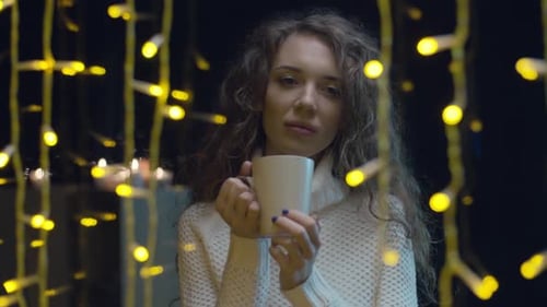 Woman Drinks Coffee Near Christmas Lights on Rainy Night